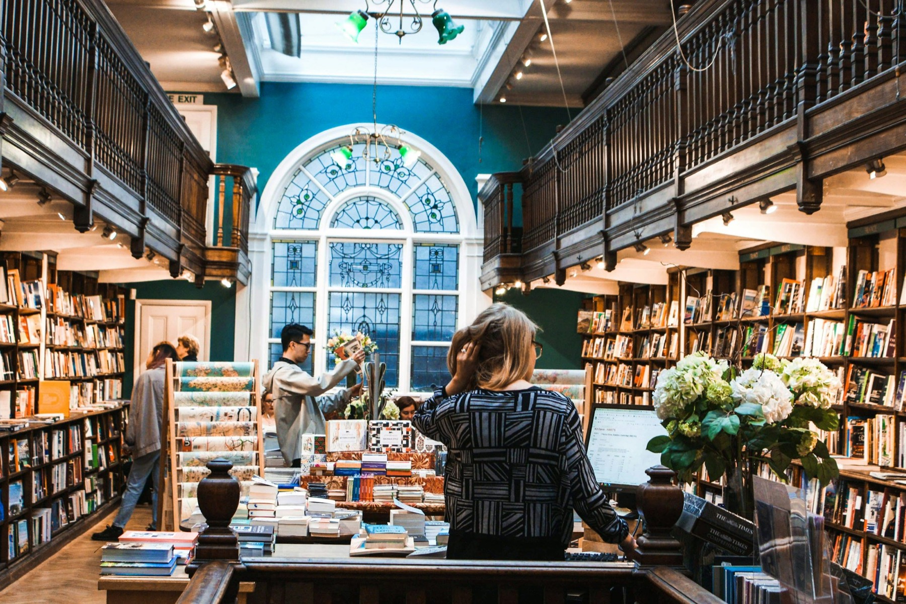 People browsing a tall, light-filled bookshop.
