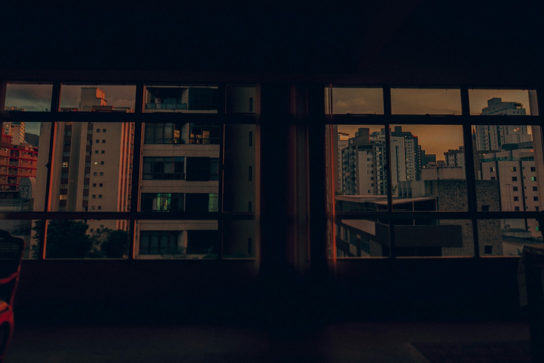 City windows lit at night, seen from a dark room.