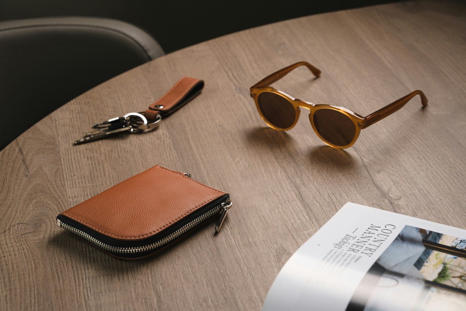 Sunglasses, keys and a leather wallet on a wooden table.