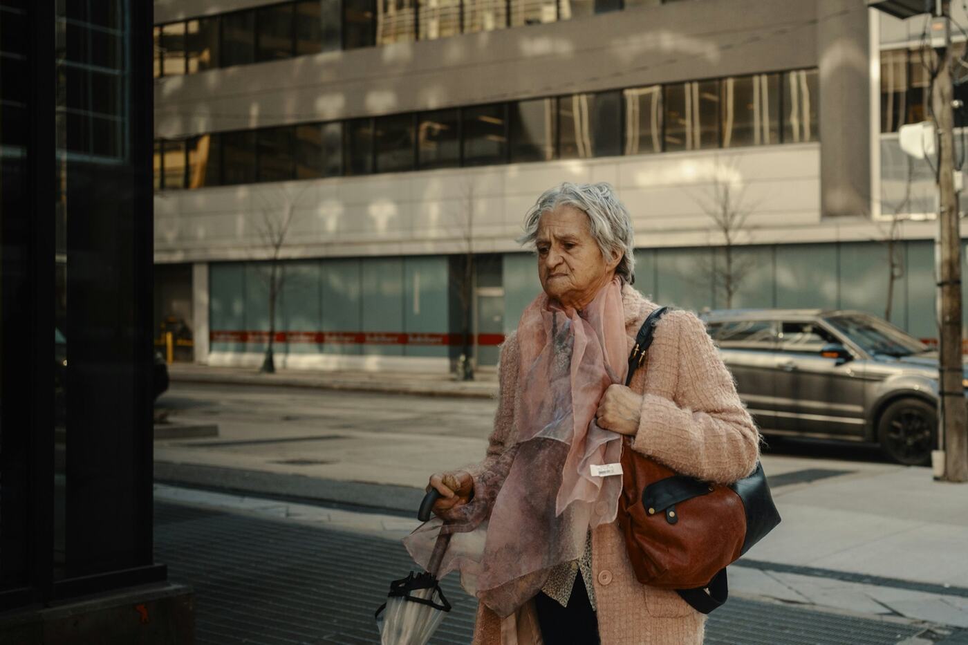 An older woman walking a city street, bag on her shoulder.